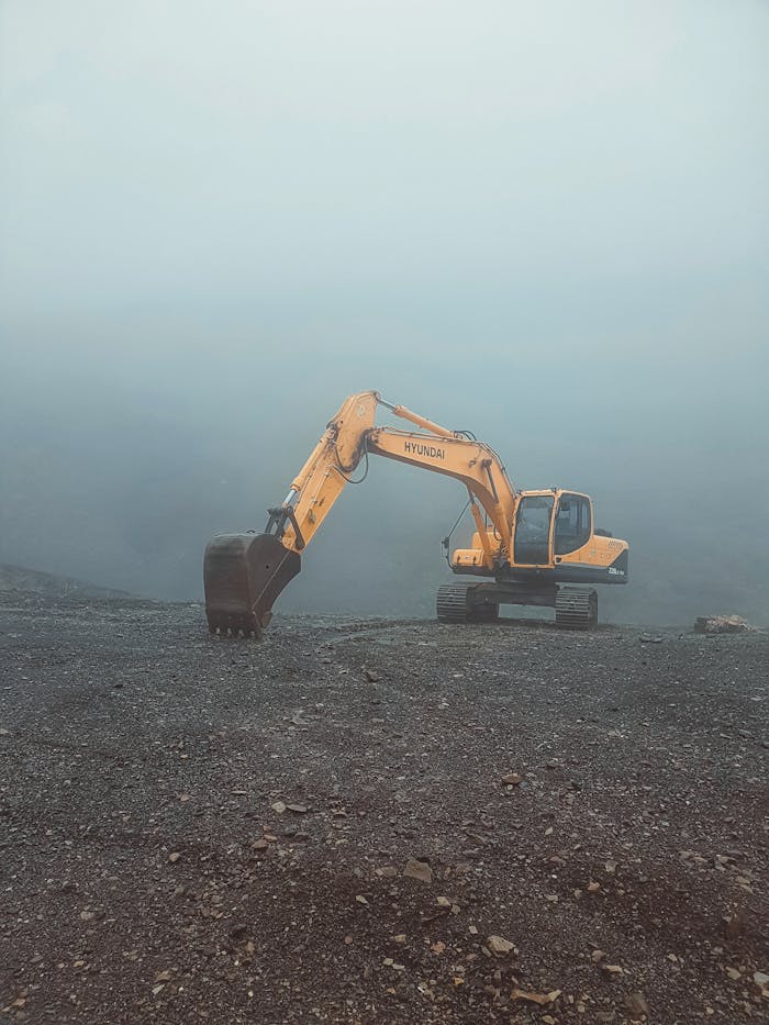 A solitary excavator on a misty day in Krasnaya Polyana, Russia, set against a barren landscape.