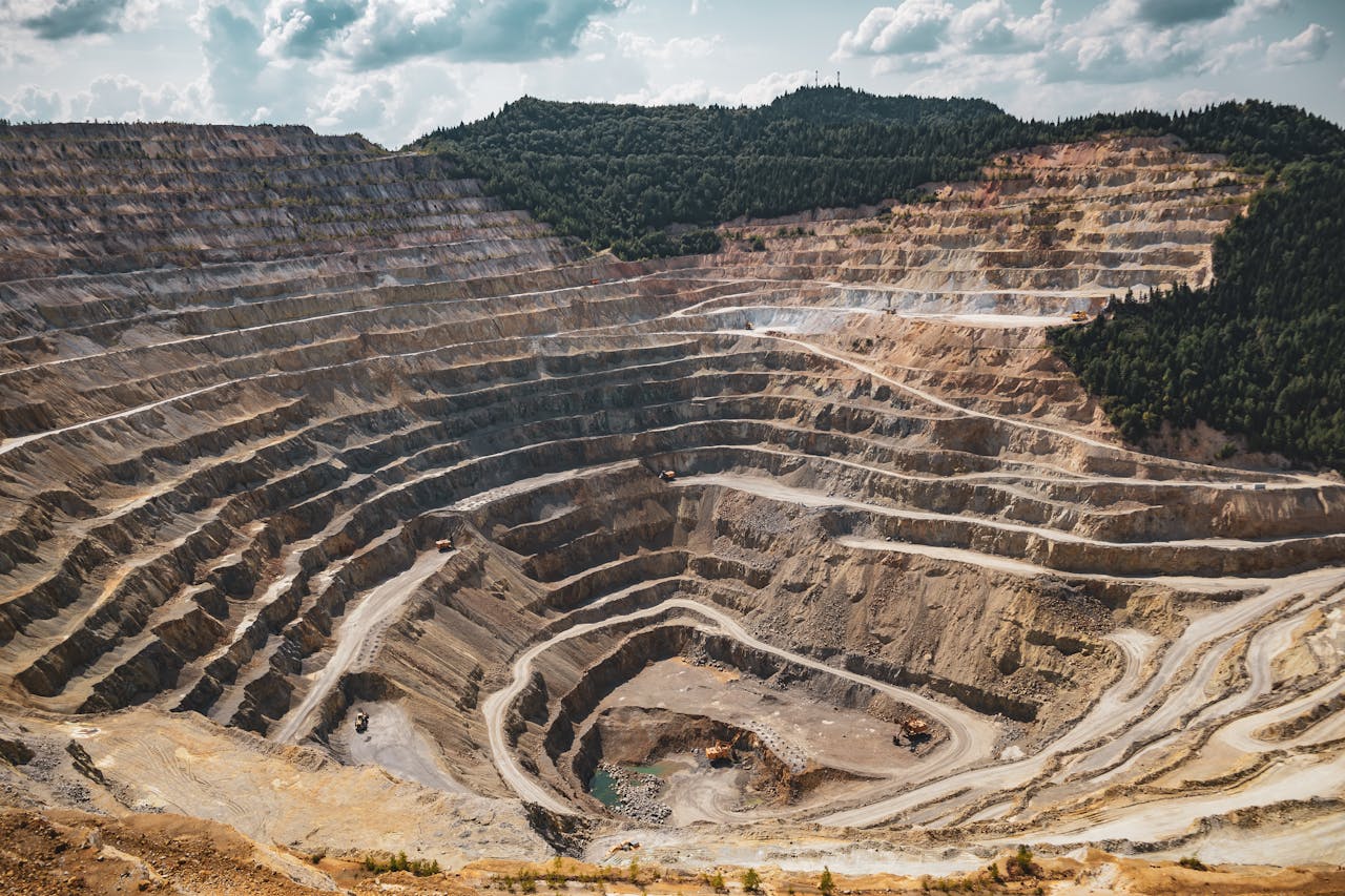 Services-03 Aerial view of a large open-pit mine with terraced excavation during summer.